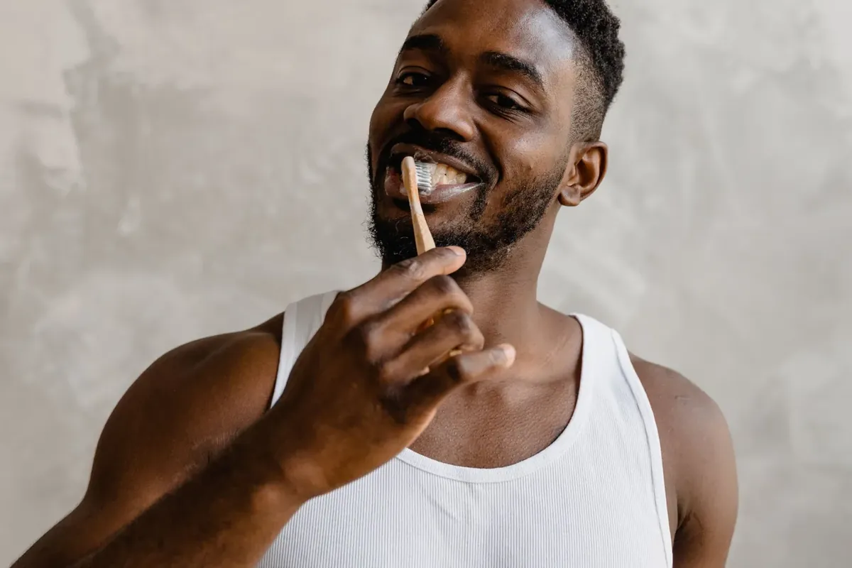 A smiling man holding a toothbrush, part of a daily oral care routine