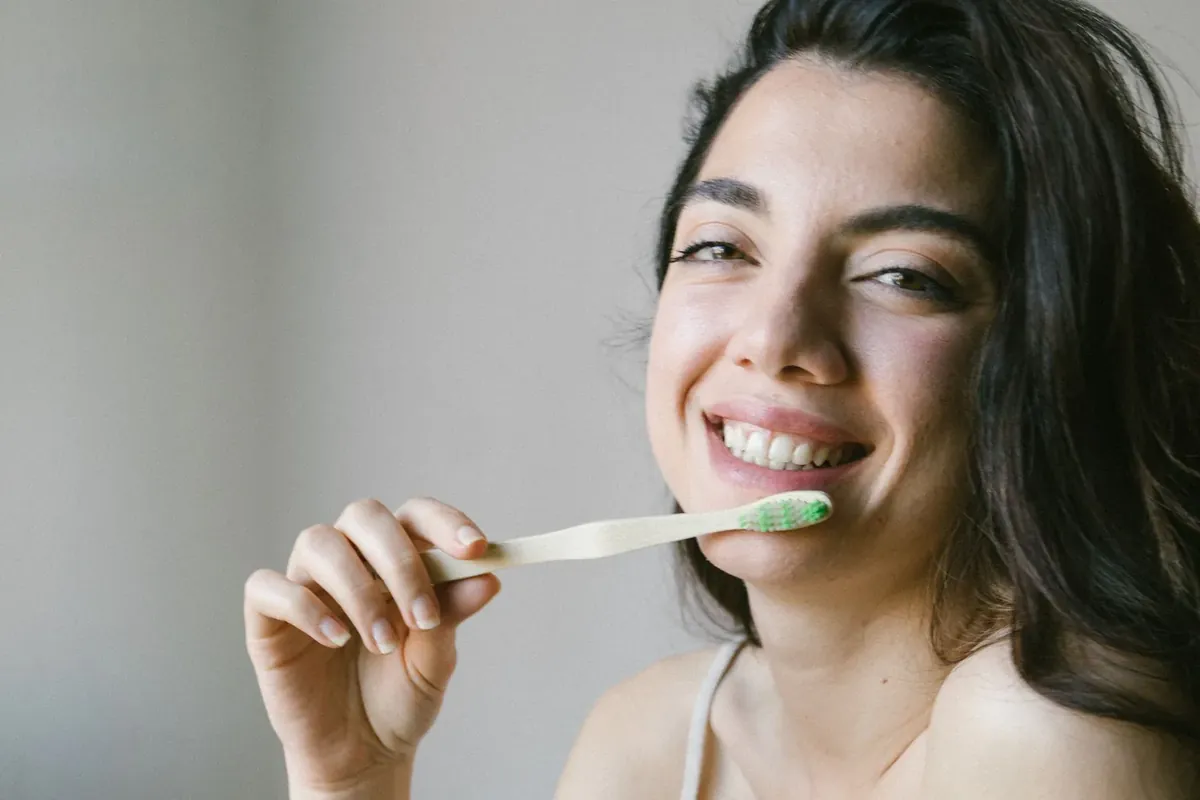 A smiling woman gently brushing her teeth with a soft toothbrush