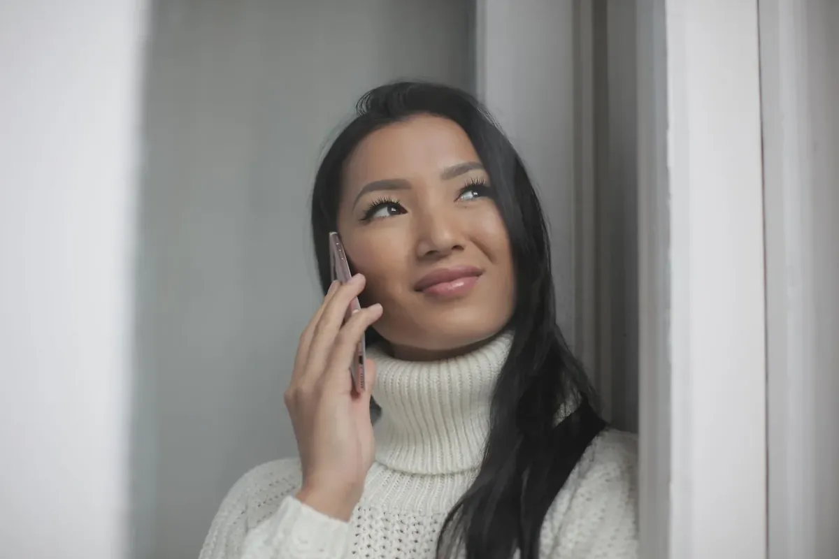 A calm young Asian woman making a phone call by the window
