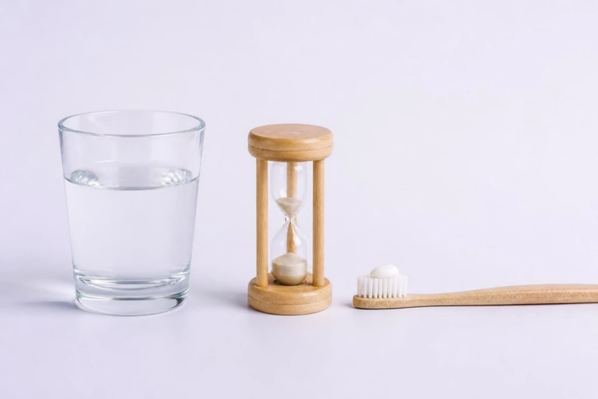 3D illustration of three things in a row: a glass of plain water, a small sand timer, and a soft toothbrush with a pea-sized dab of toothpaste