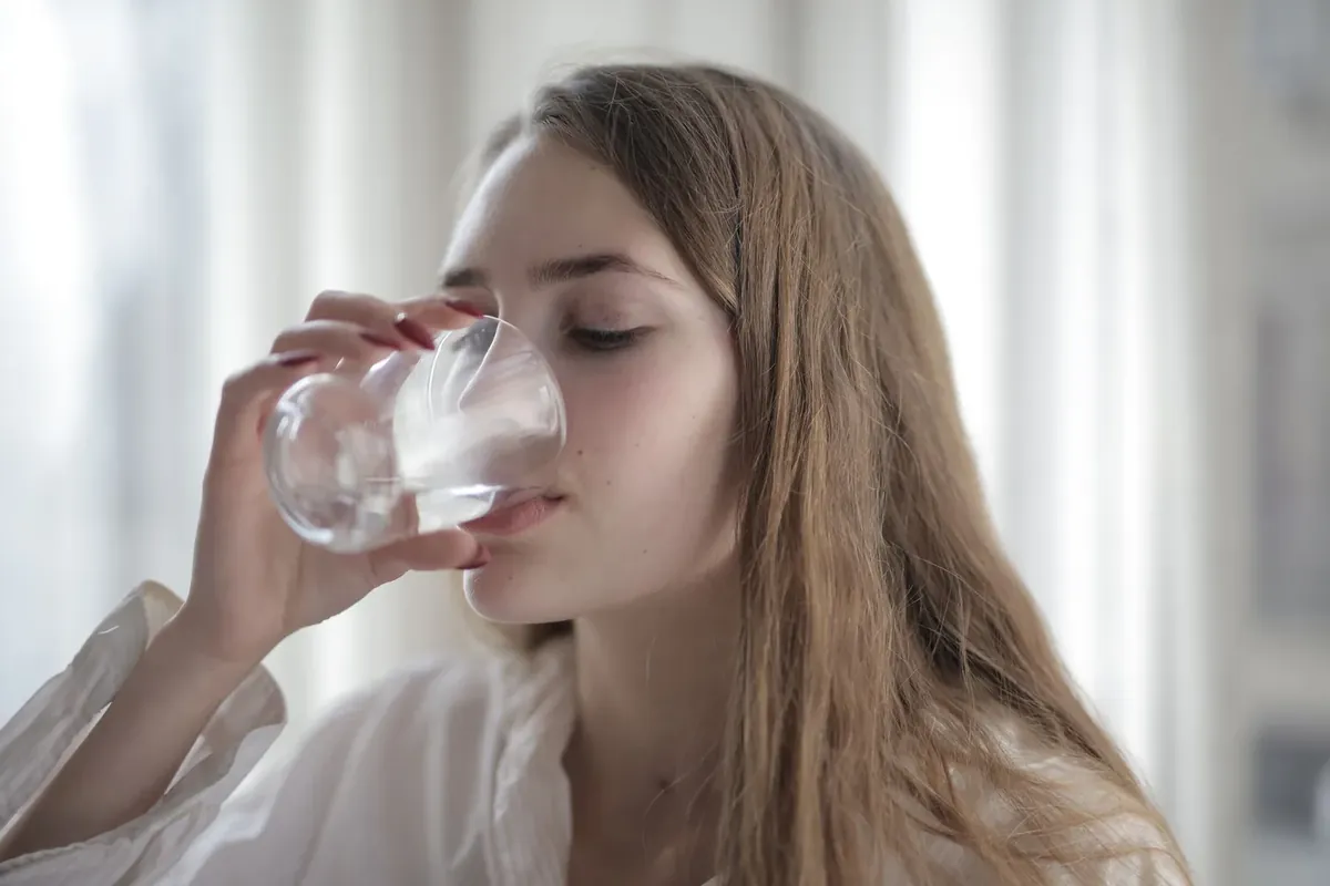 A woman drinking a glass of water, which helps with a dry mouth