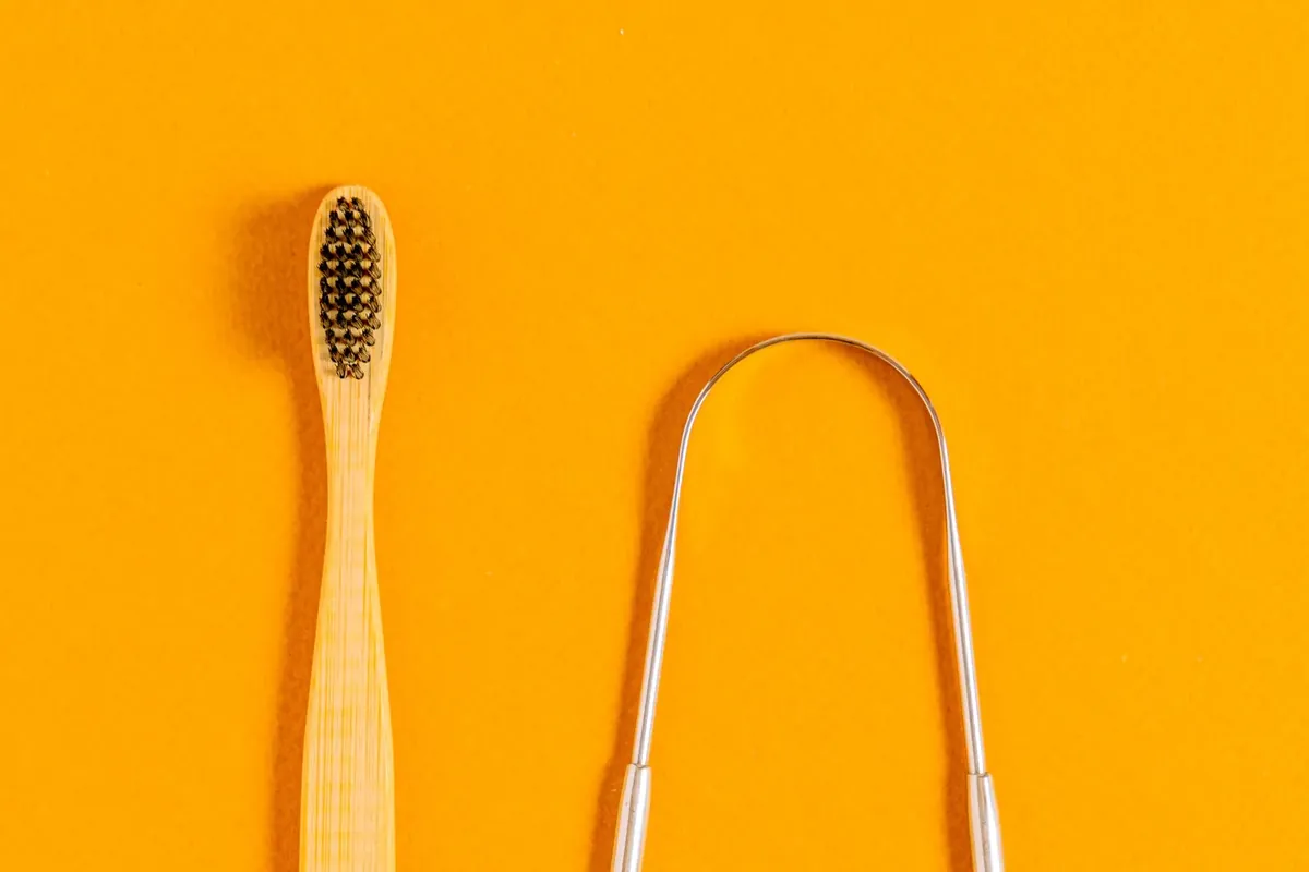 A metal tongue scraper next to a bamboo toothbrush