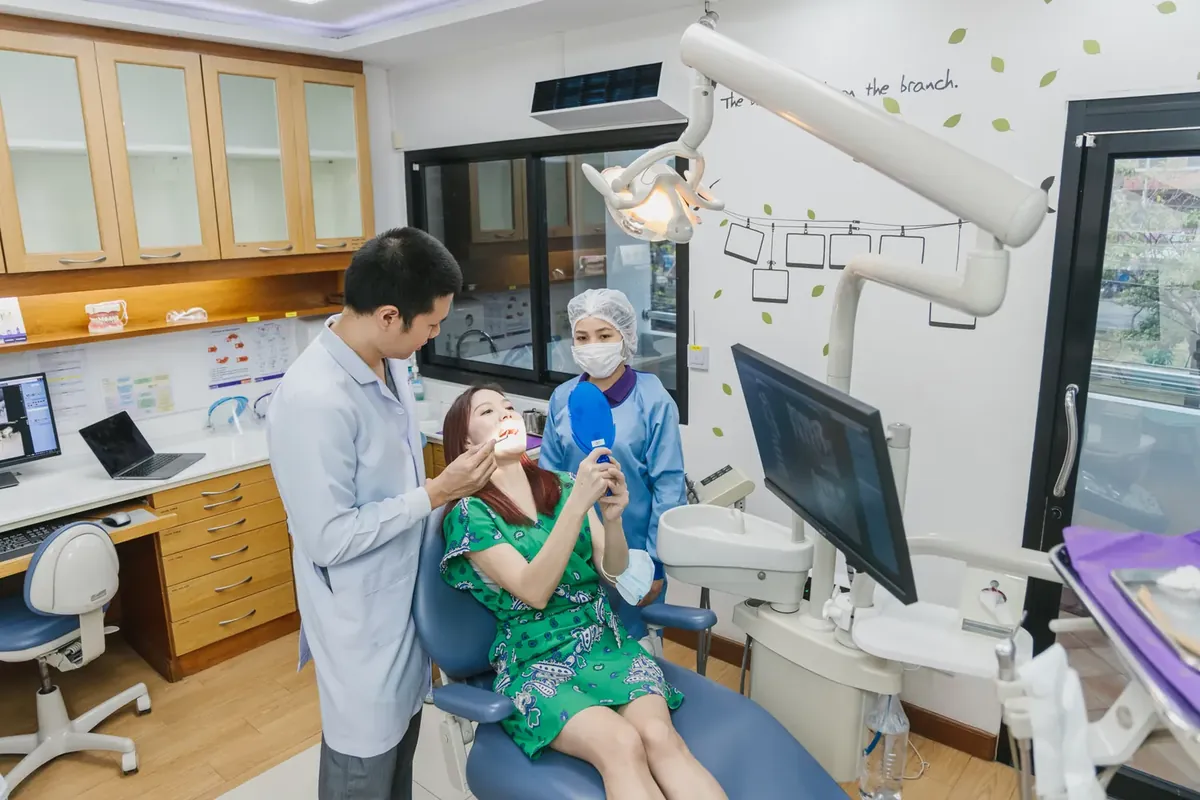 A dentist explaining a gum check to a patient holding a hand mirror in the dental chair