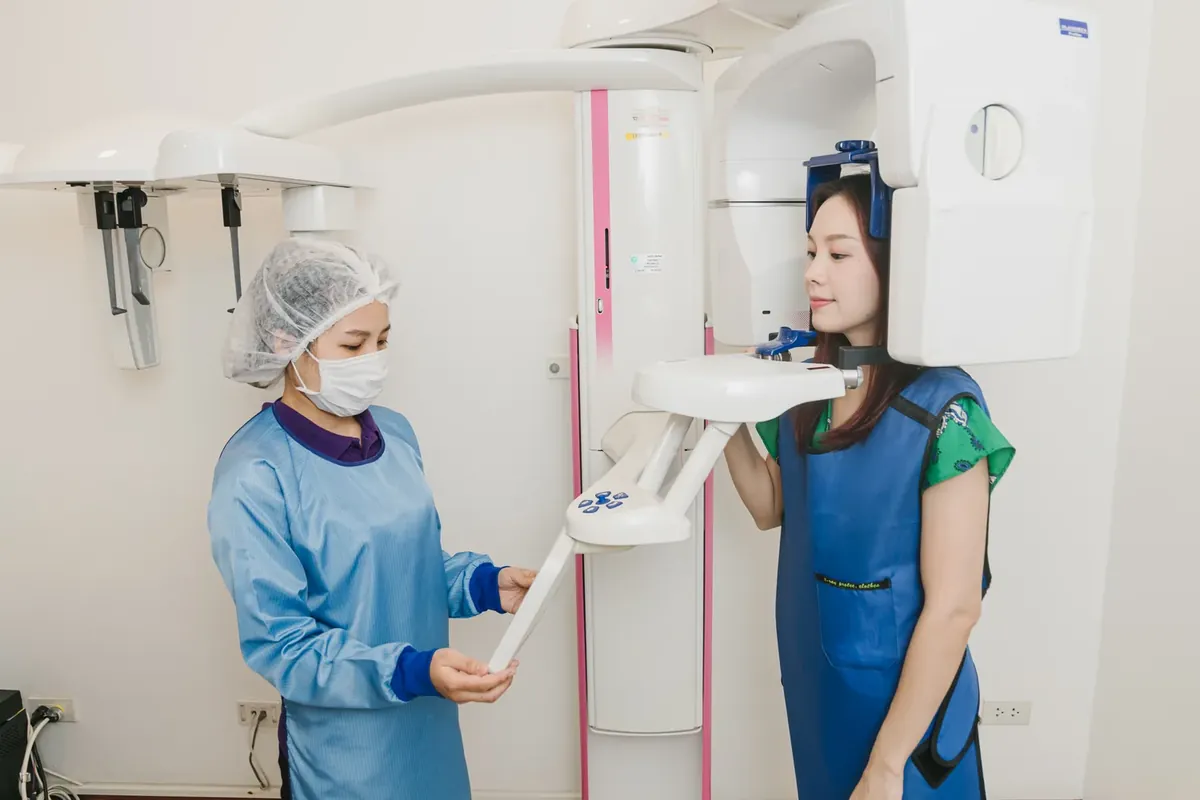 A dental assistant positioning a smiling patient in a lead apron at the CBCT 3D scanner