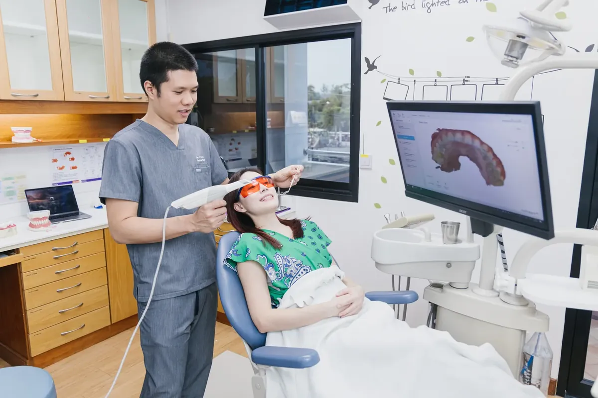 A dentist scanning a patient’s teeth with an intraoral scanner while the 3D model shows on screen
