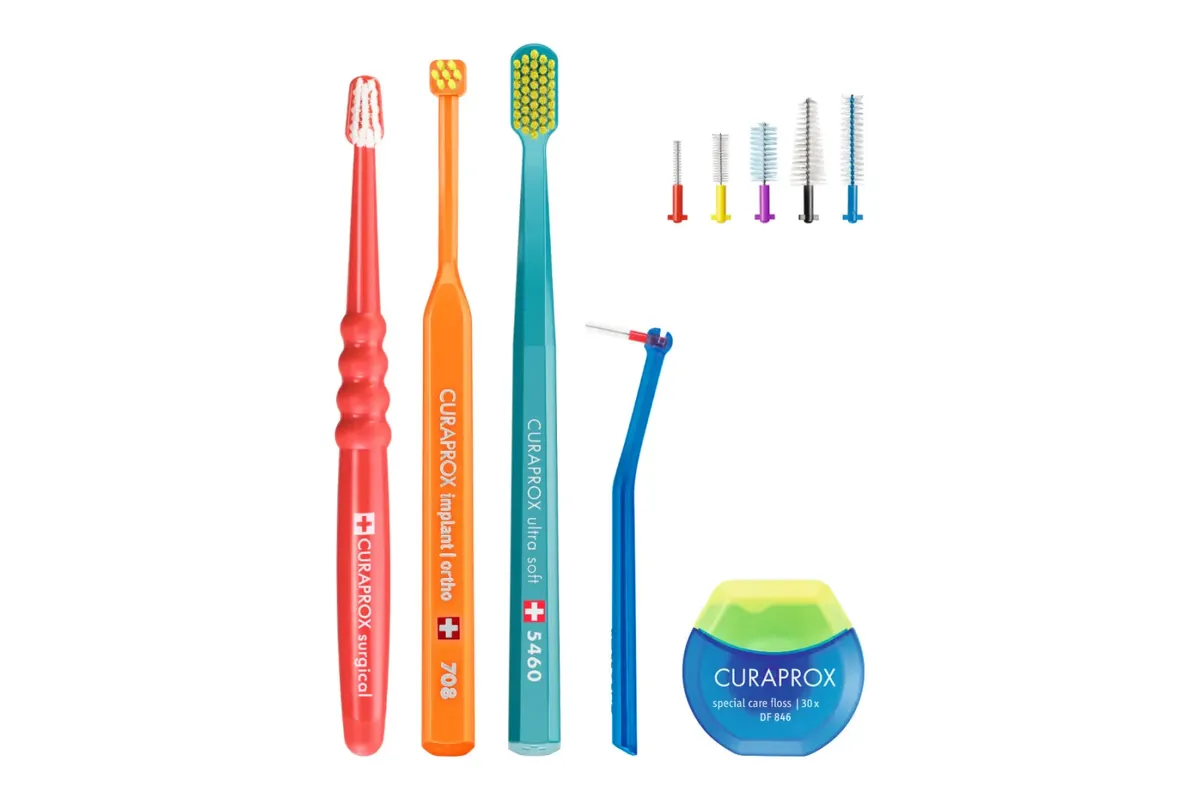 A set of cleaning tools on white: three soft toothbrushes, one of them with a small head, five interdental brushes in different sizes, an interdental brush on an angled handle and a round box of floss