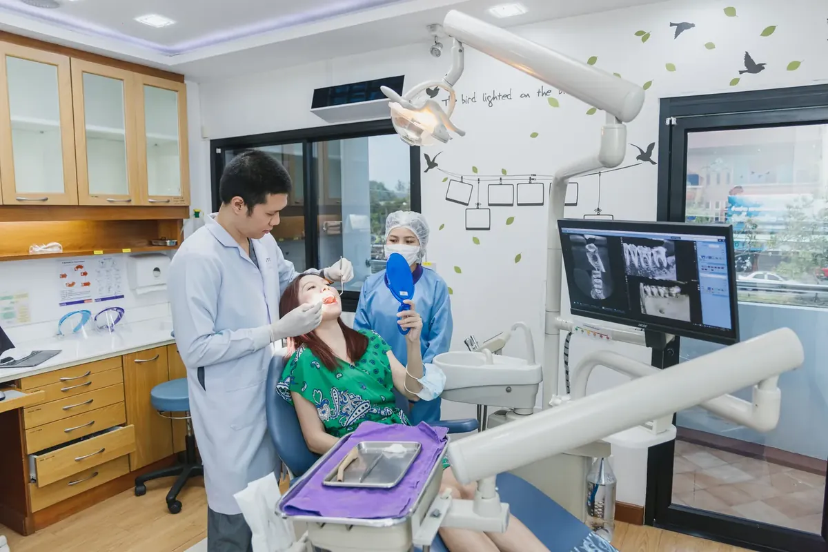 A dentist examining a patient with an assistant, with an X-ray image on the screen