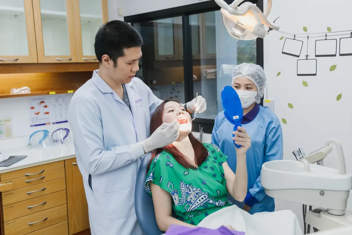 A dentist examining a smiling patient who holds a hand mirror