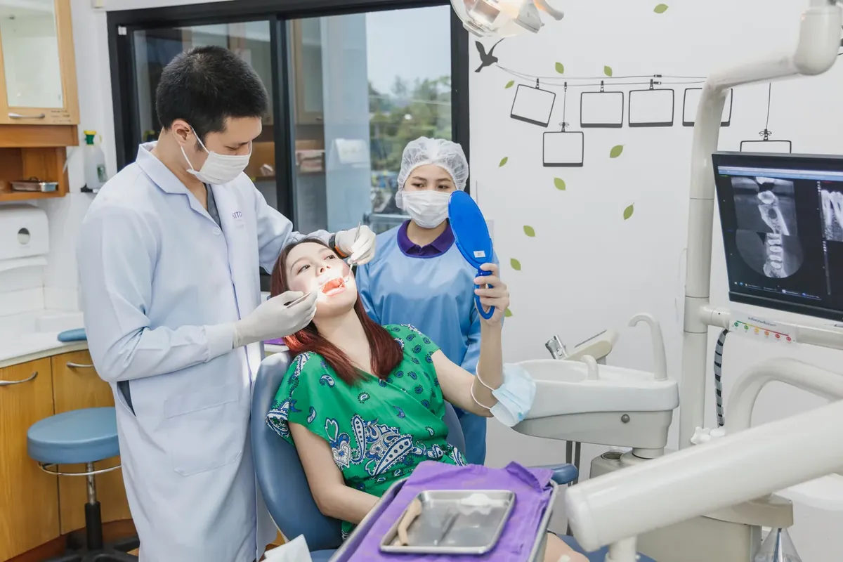 A dentist examining a patient with a panoramic X-ray on the screen behind