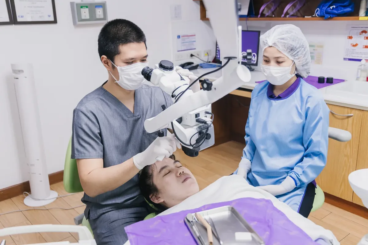 A dentist treating a tooth under a dental operating microscope