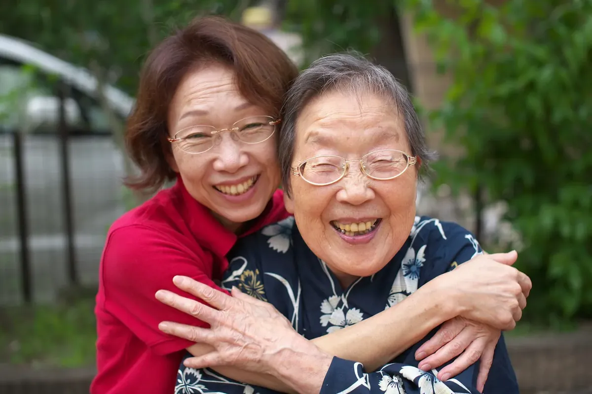 An adult daughter hugging her smiling elderly mother outdoors