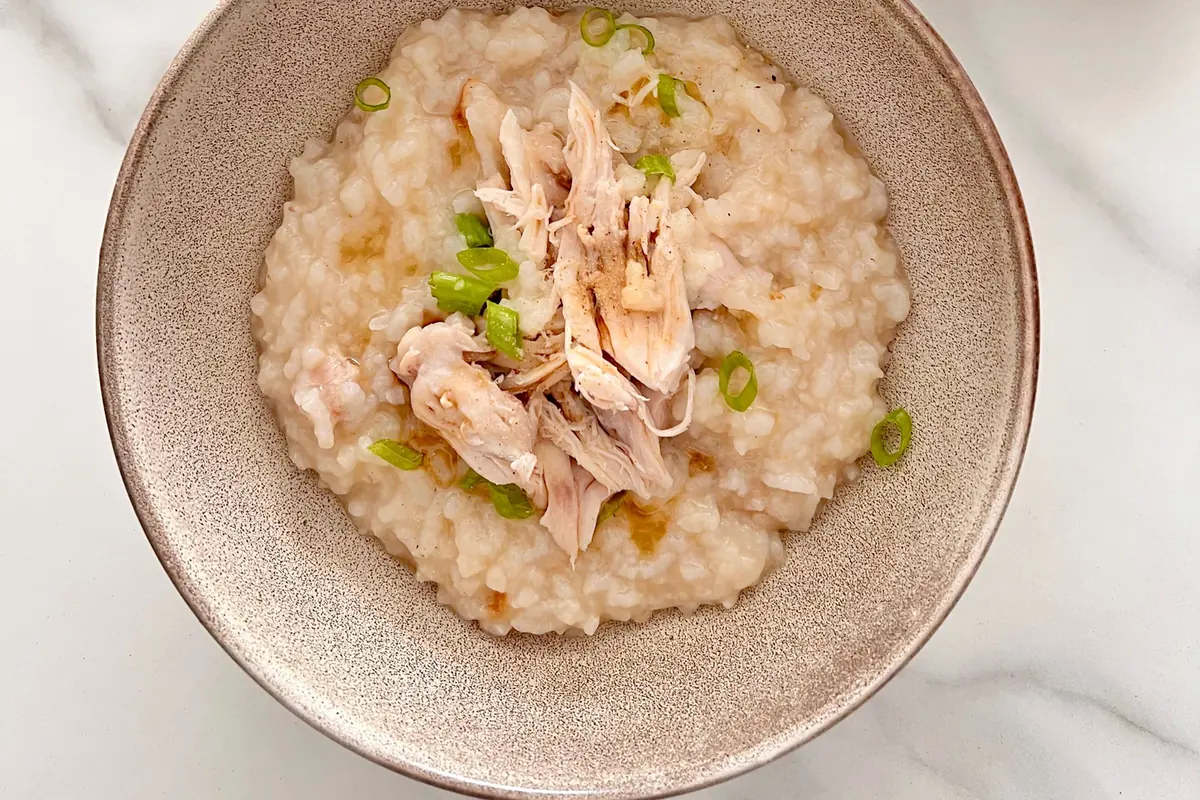 A bowl of soft rice porridge with shredded chicken and spring onion