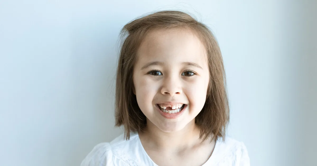 A cheerful young girl smiling and showing a gap where a baby tooth has fallen out