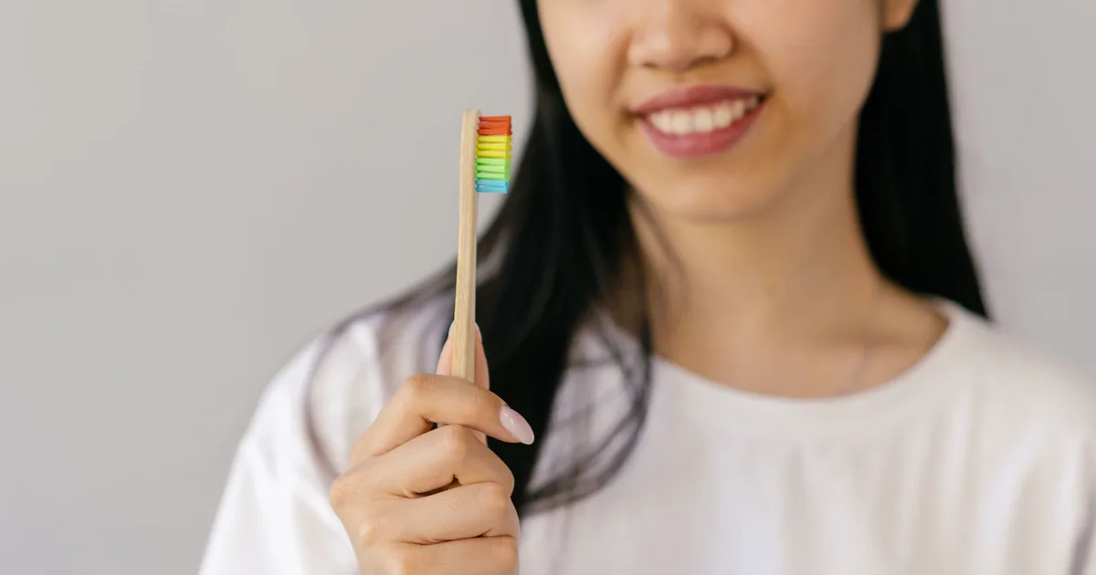 A smiling young woman holding a bamboo toothbrush
