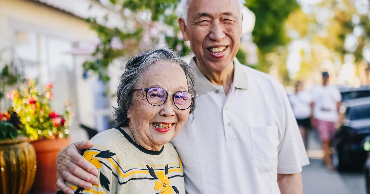 A happy senior Asian couple smiling together outdoors, holding flowers