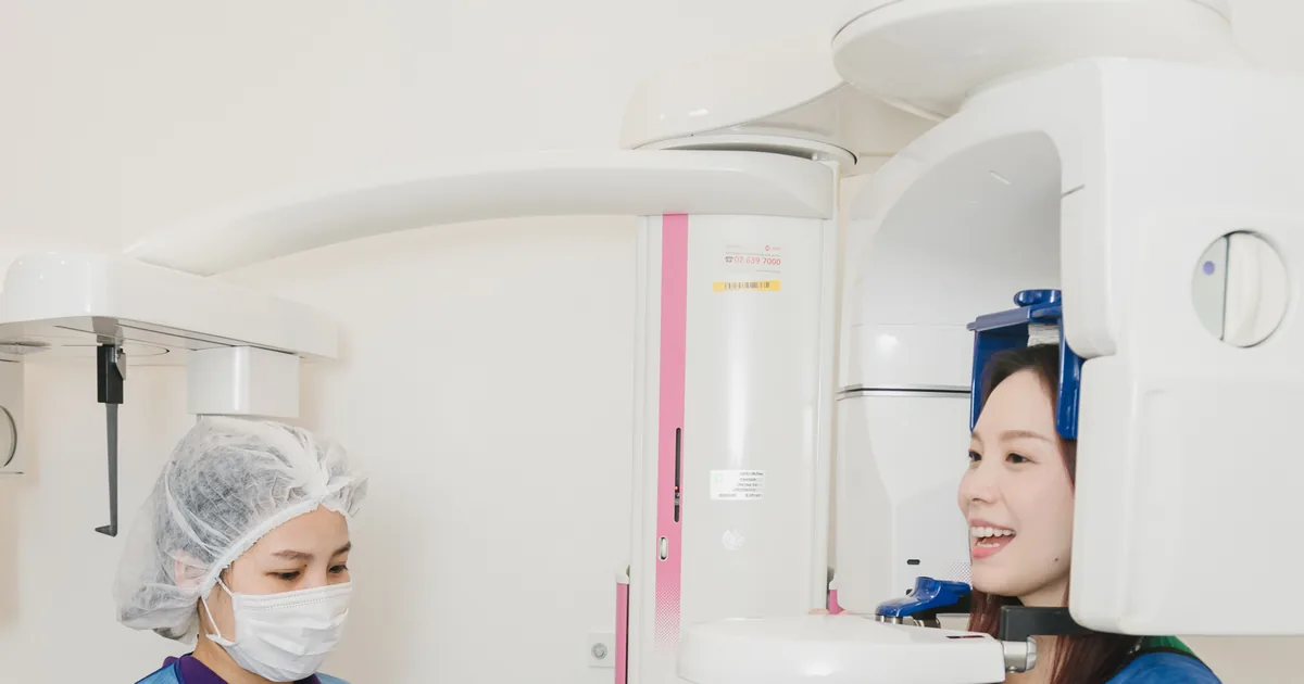 A dental assistant positioning a smiling patient in a protective apron at the CBCT 3D scanner