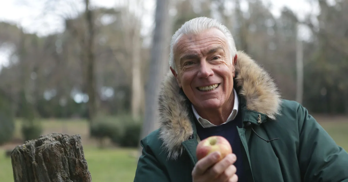 A smiling older man holding a fresh apple outdoors