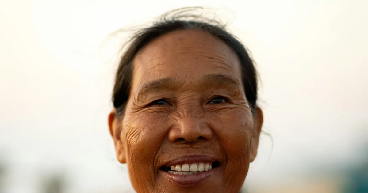 An elderly Asian woman in a purple jacket smiling warmly