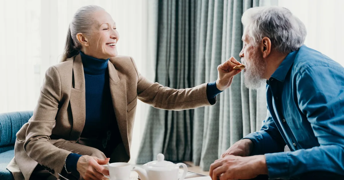A smiling senior couple sharing tea and cake at home