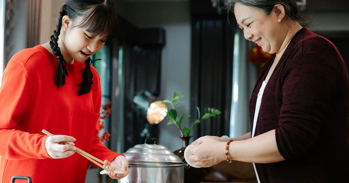 A smiling grandmother and her granddaughter making dumplings together at home