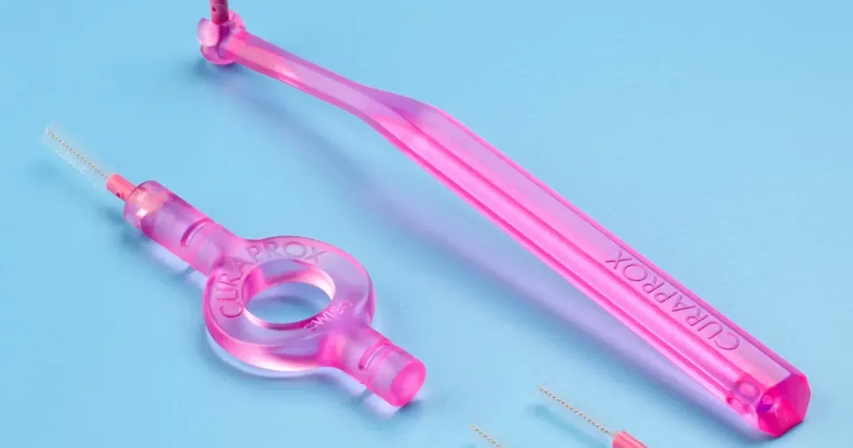 A pink interdental brush with an angled handle and a ring-shaped holder, with spare brush heads, on a light blue background