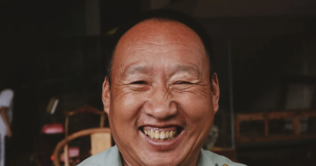 A cheerful middle-aged Asian man smiling broadly indoors
