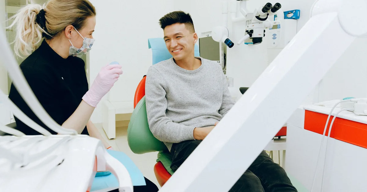 A young man laughing in the dental chair while talking with his dentist