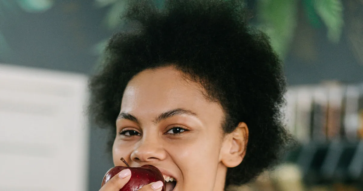 A smiling young woman taking a confident bite of a red apple