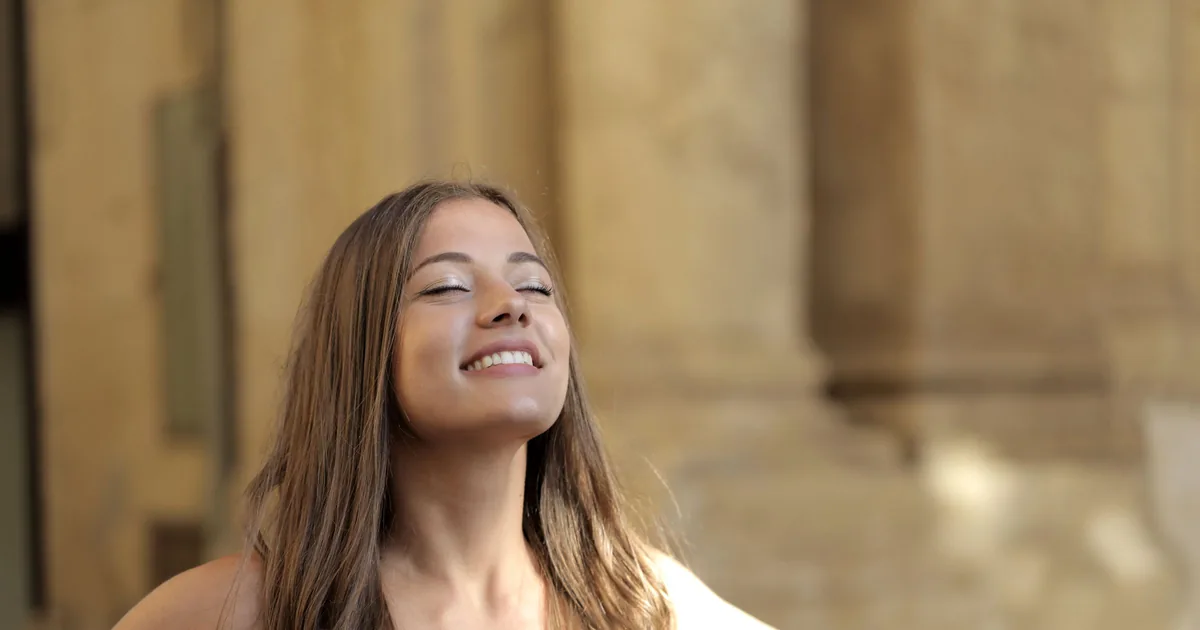 A smiling woman with eyes closed enjoying warm sunlight, relaxed