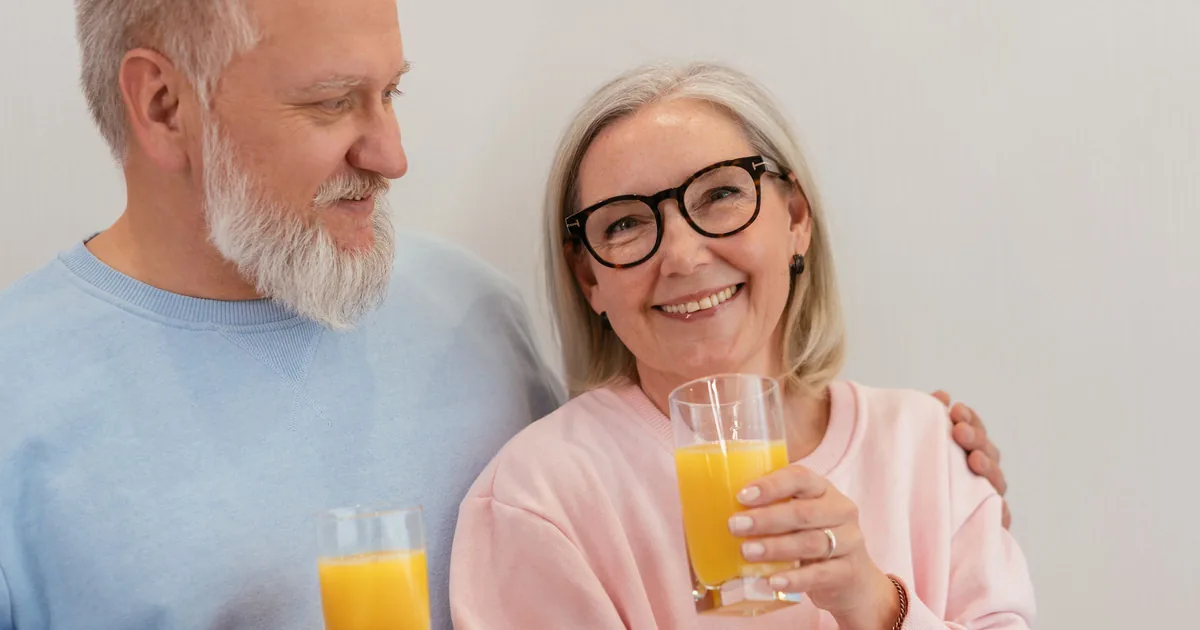 A smiling senior couple holding glasses of orange juice at home