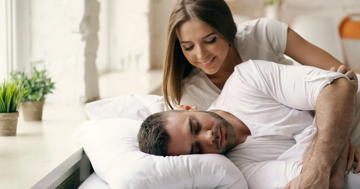 A woman smiling beside her partner as he sleeps peacefully