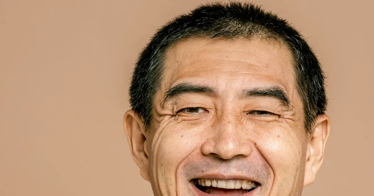 A cheerful middle-aged Asian man laughing against a warm background