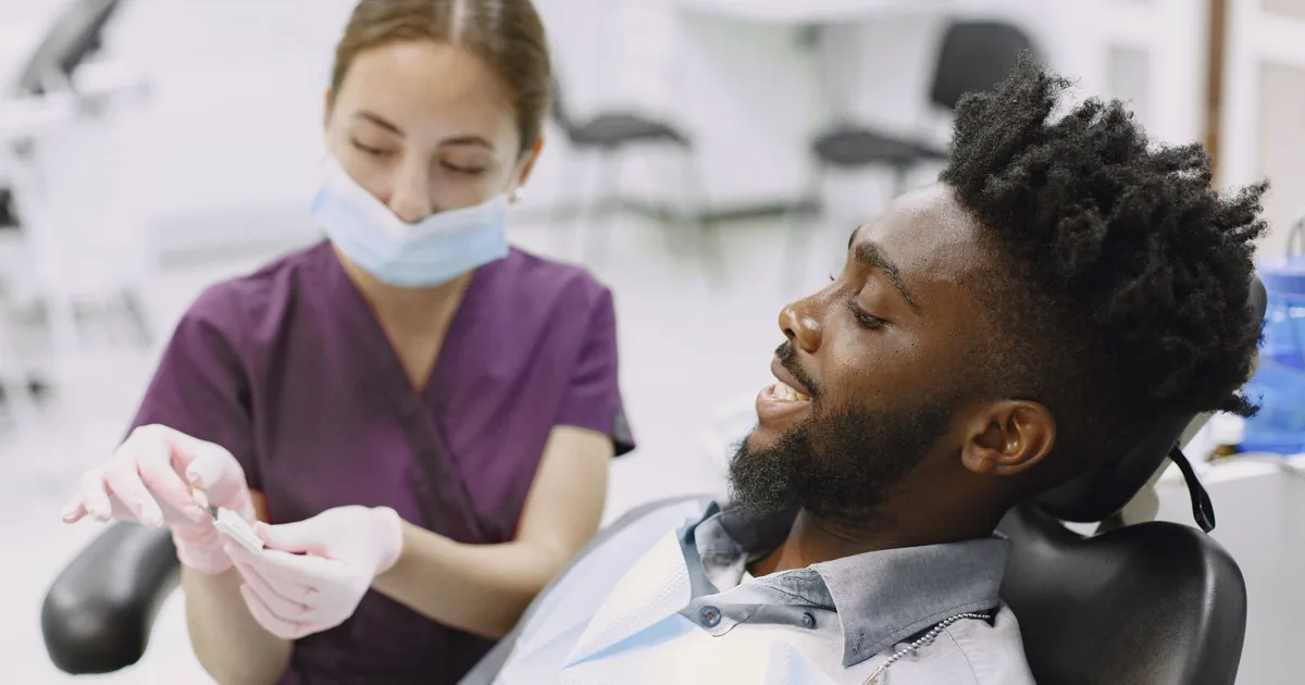 A relaxed smiling patient in the dental chair while a dental assistant in plum scrubs prepares for a check-up