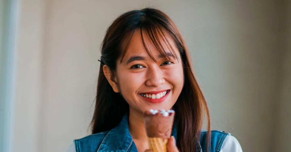 A smiling Asian woman enjoying an ice cream cone
