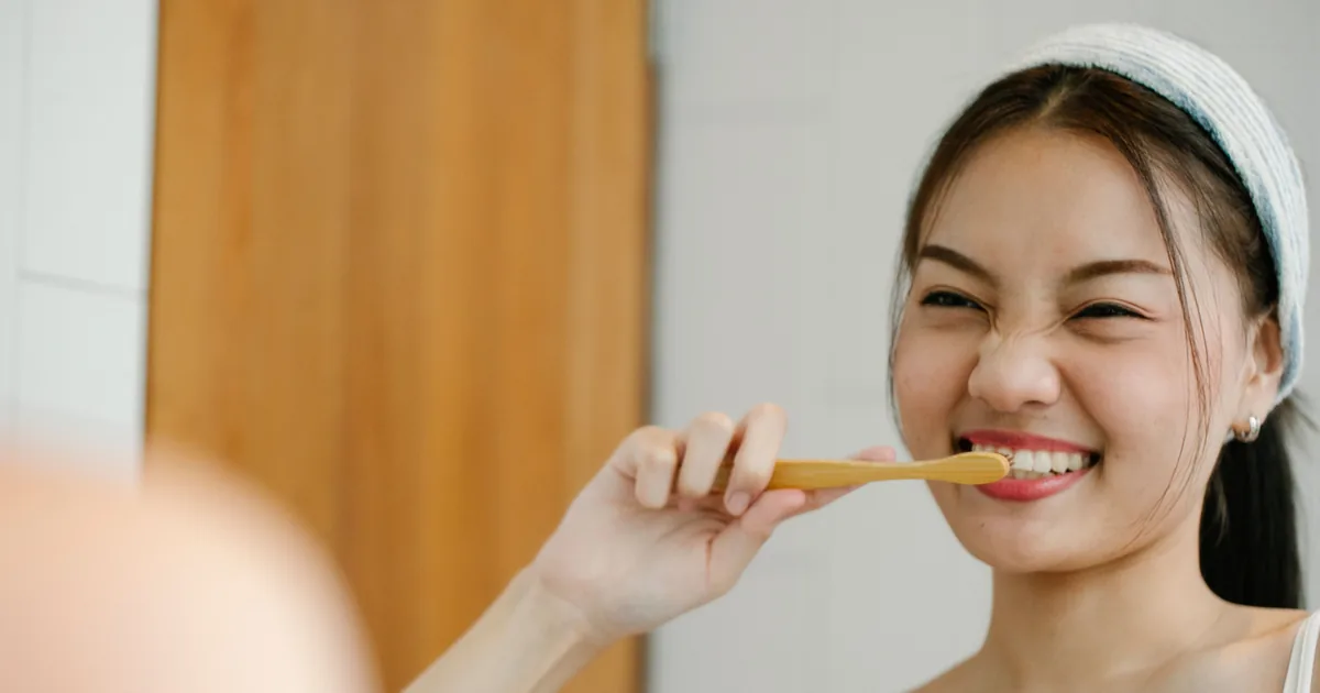 A smiling young woman brushing her teeth with a bamboo toothbrush