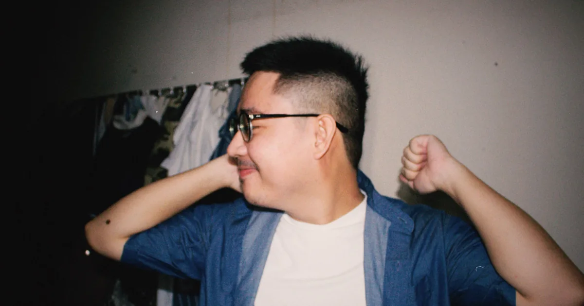 A cheerful young Asian man in glasses smiling and relaxing indoors