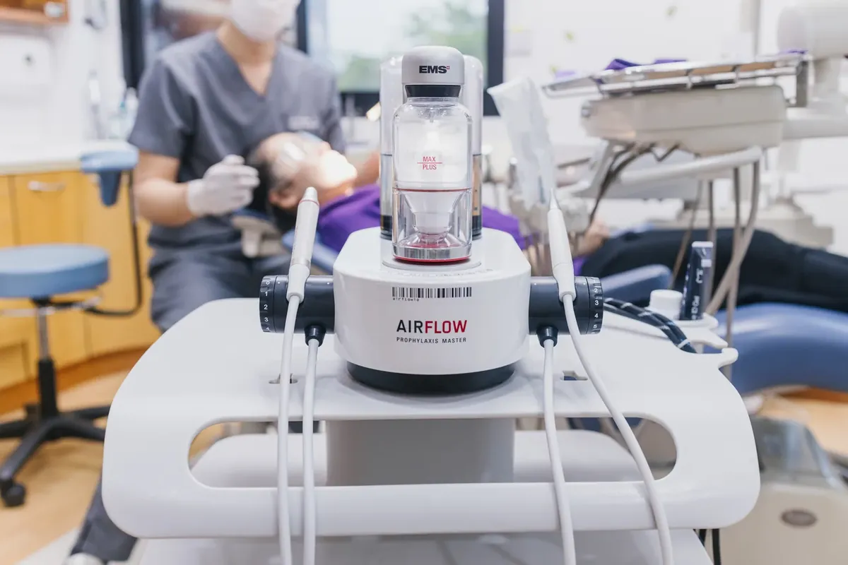 An Airflow cleaning unit in the foreground while a dentist cleans a patients teeth behind it