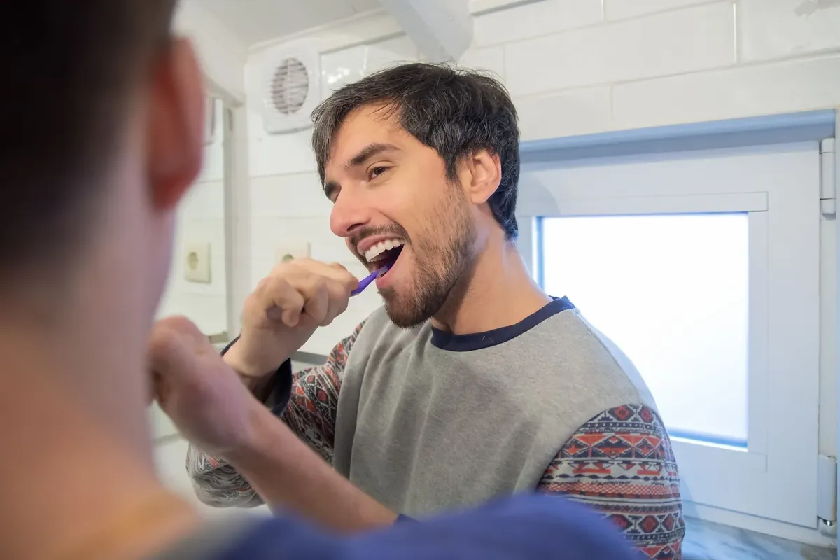 A man brushing his teeth in the bathroom mirror as part of his daily routine