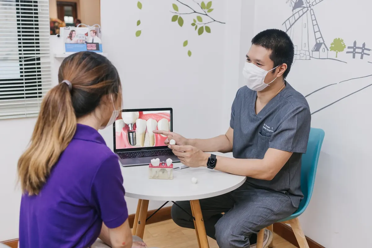 A dentist explaining an implant tooth with a picture on a laptop and an implant model on the table