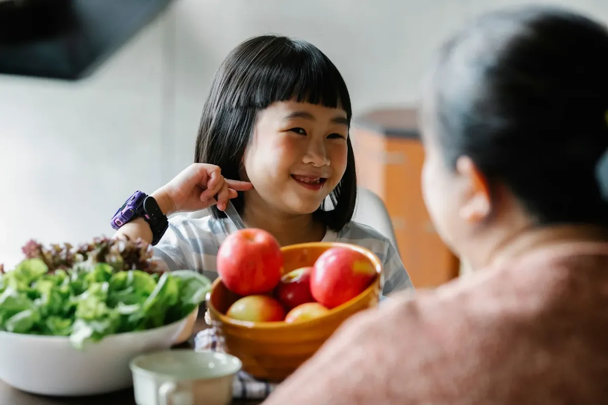 A smiling girl eating fruit and vegetables with her mother