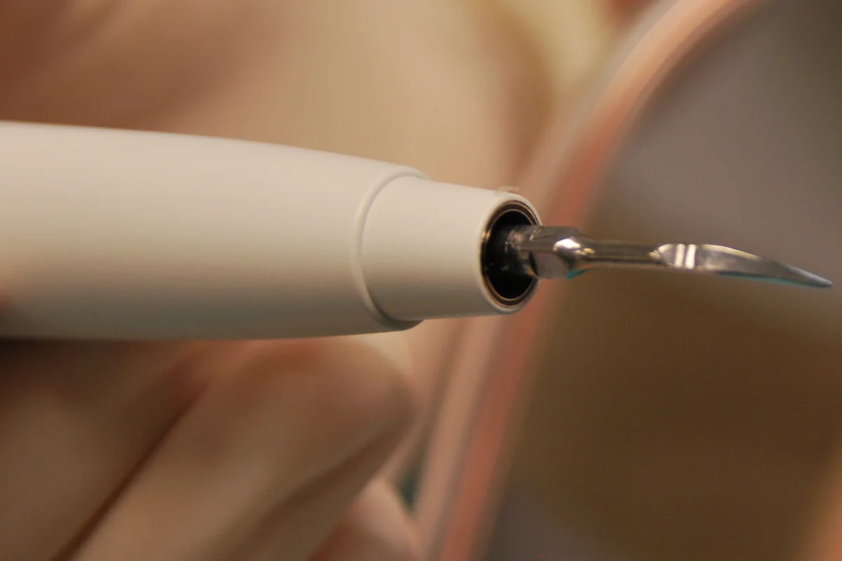 Close-up of the handpiece of an ultrasonic scaler with its thin curved metal tip, the tool used to remove tartar