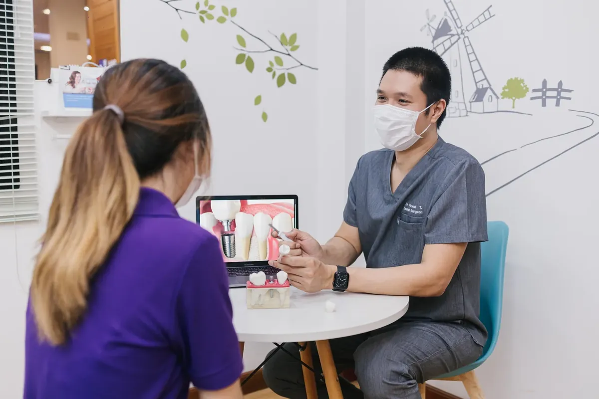 A dentist explaining a dental implant on a laptop with an implant model on the table