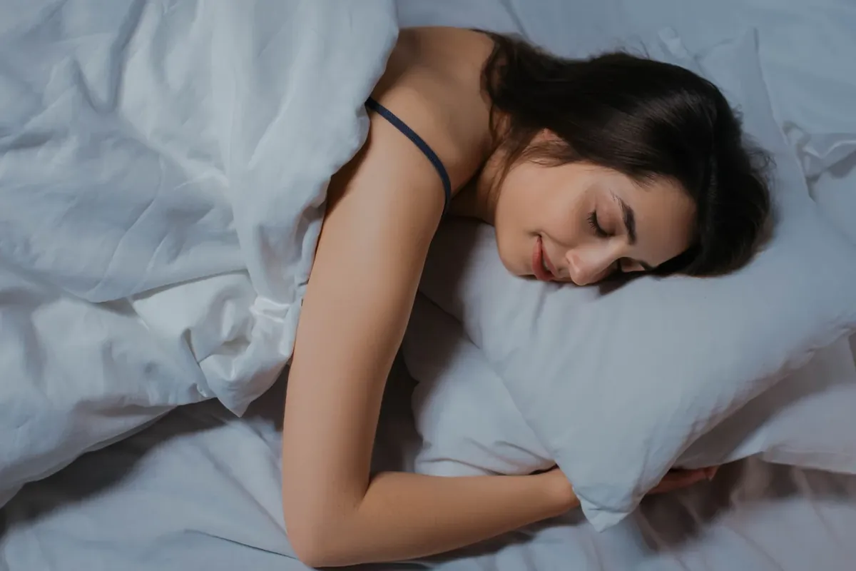 A woman sleeping peacefully in a bed with white linen