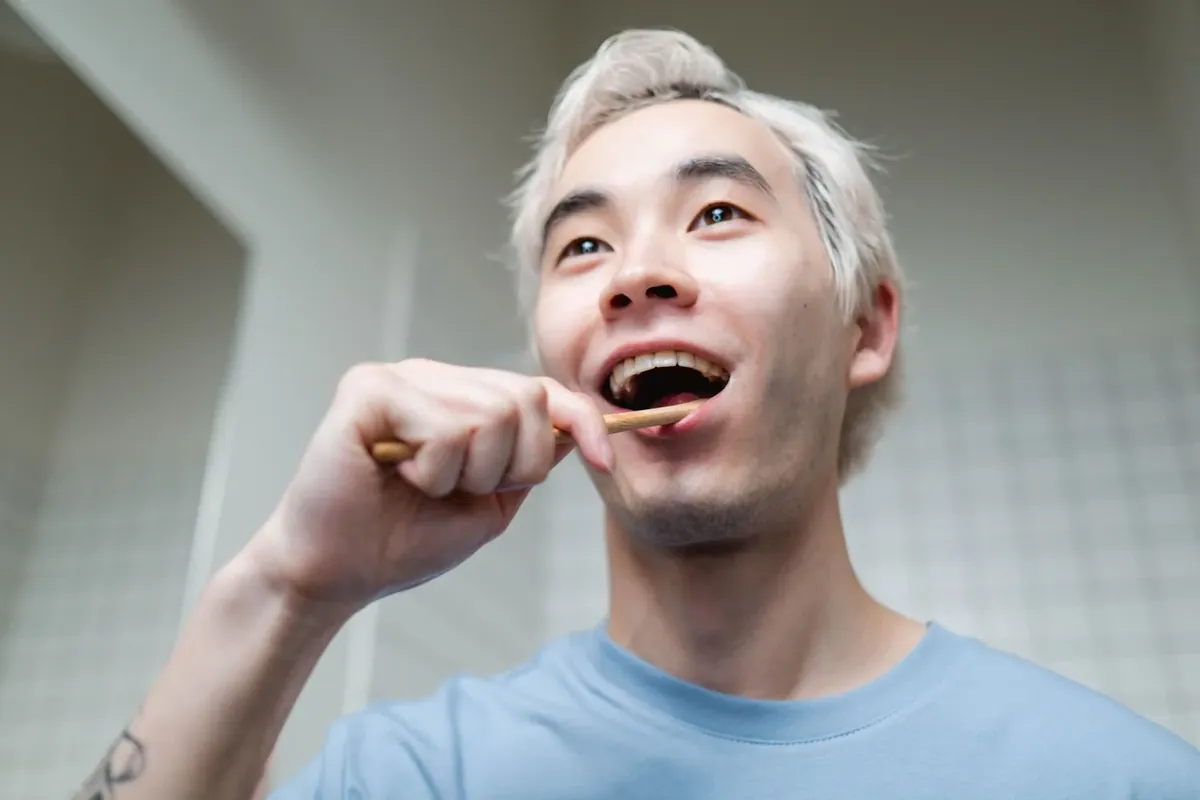 A smiling man brushing his teeth with a bamboo toothbrush