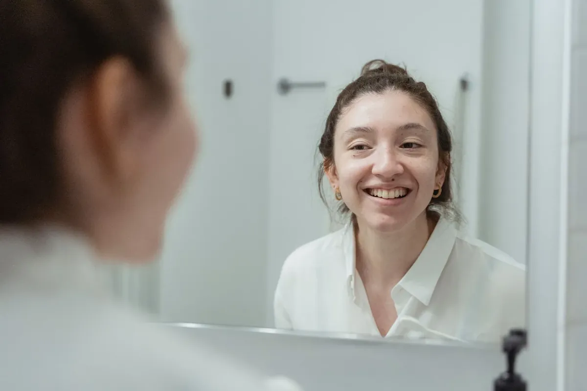 A smiling woman checking her teeth and gums in the bathroom mirror