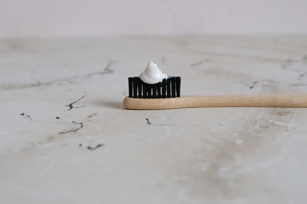 A bamboo toothbrush with a small amount of toothpaste on a marble surface