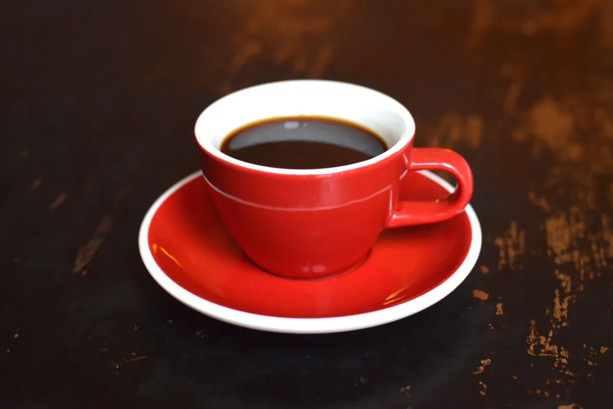 A cup of black coffee in a red cup and saucer on a dark wooden table