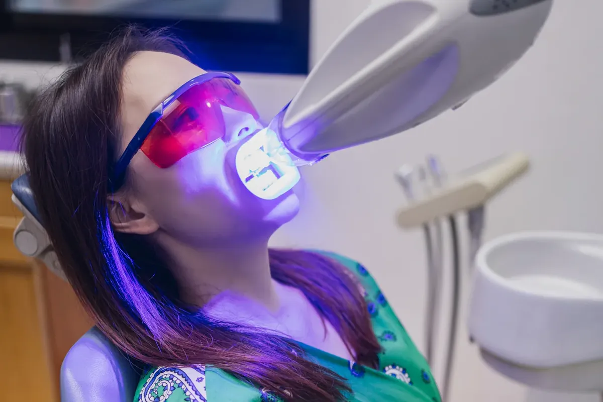 A patient wearing orange protective glasses relaxing while a whitening light shines on her teeth